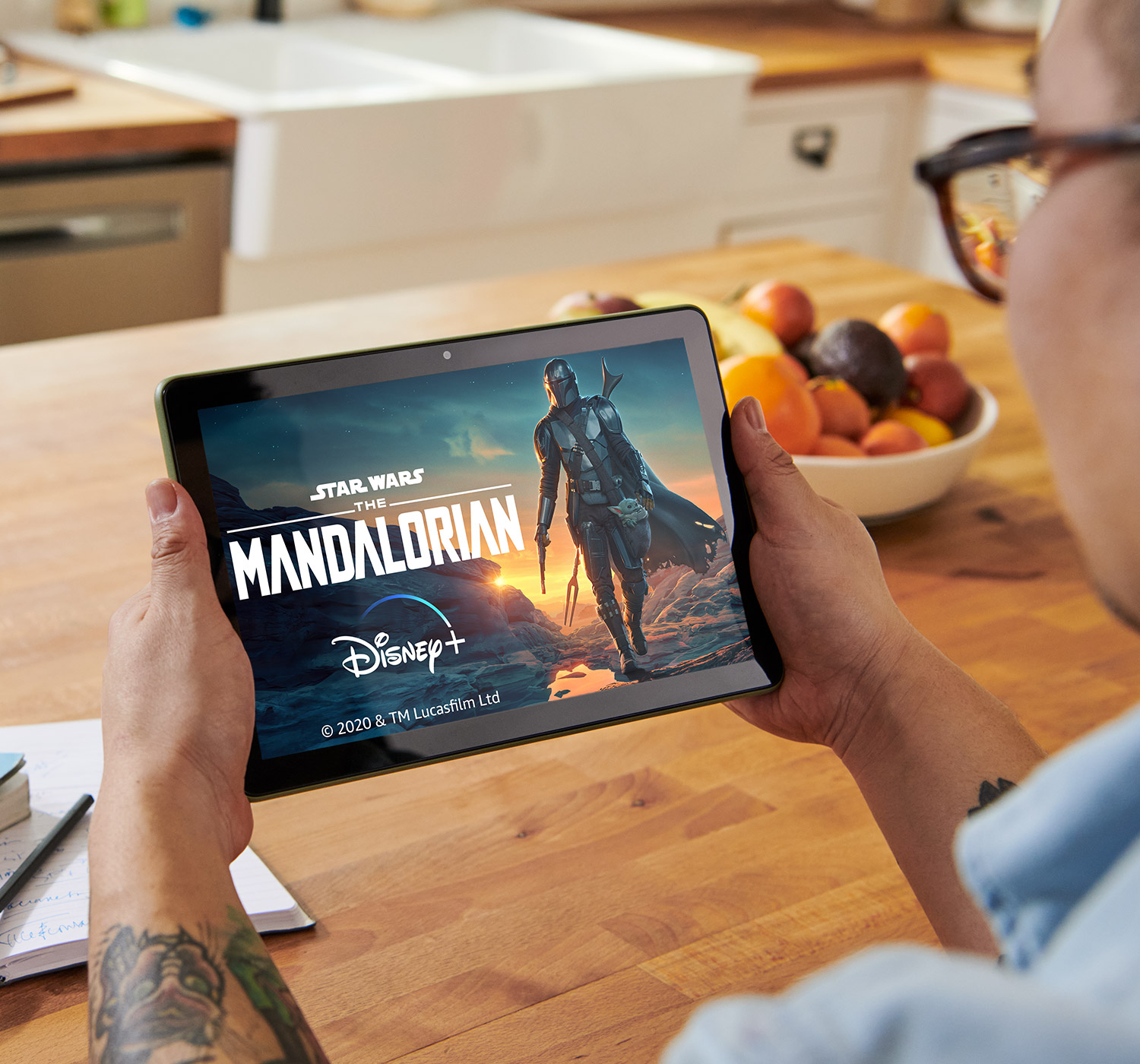 A man is watching The Mandalorian on his Fire HD 10 tablet while seated in the kitchen.