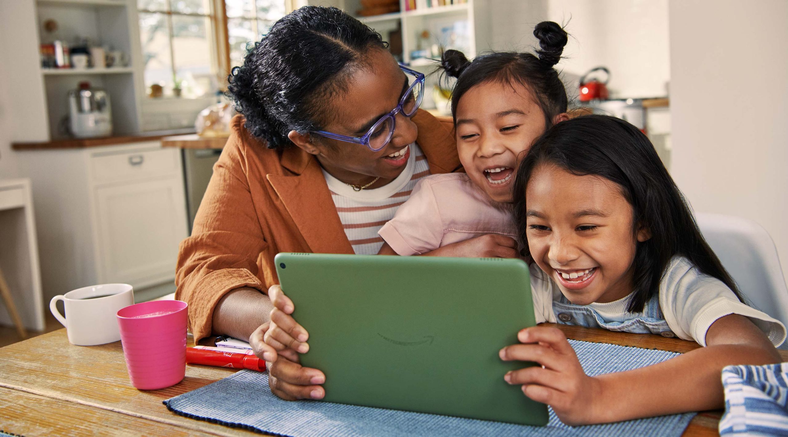 An adult and 2 children looking at Fire HD 10 and laughing while seated in the kitchen.